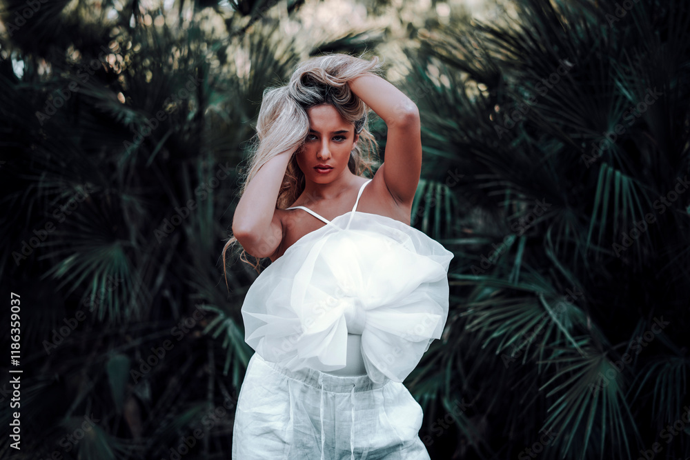 Chica rubia joven posando en jardin con traje blanco