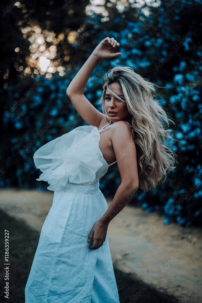 Chica rubia joven posando en jardin con traje blanco