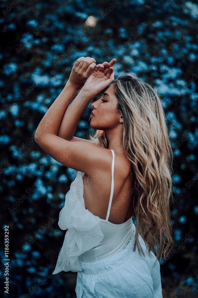 Chica rubia joven posando en jardin con traje blanco