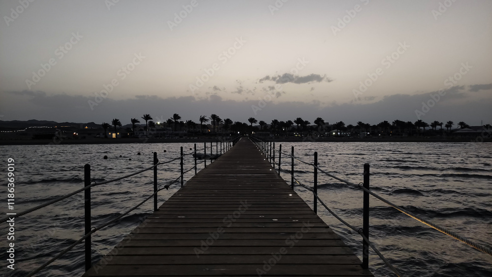 Fototapeta premium Wooden pier stretching into the calm sea at dusk in marsa alam, egypt