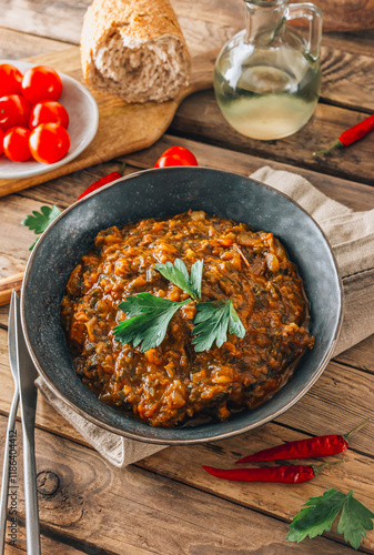 Traditional Georgian dish Ostri in a black bowl with meat pieces, vegetables, and herbs, surrounded by ingredients on rustic wooden table. Selective focus photo