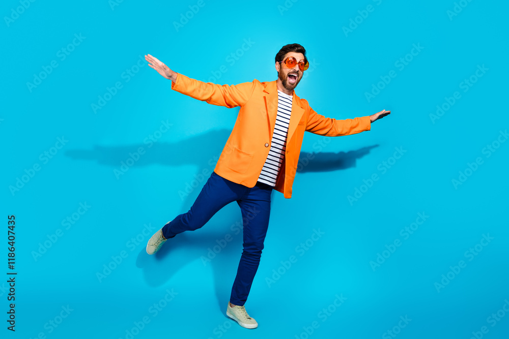 Obraz premium Stylish young man in an orange jacket and striped shirt joyfully posing against a bright teal background