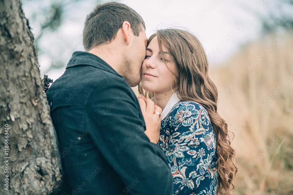 Fototapeta premium A couple is hugging under a tree, with the man kissing the woman's neck. Scene is romantic and intimate
