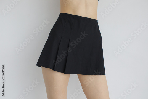 Close-up of a pleated black mini skirt on a model, showcasing its classic A-line design. Minimal background emphasizes the garment’s style, perfect for fashion catalogs or design inspiration photo