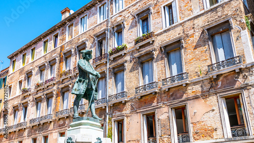 A bronze statue of Carlo Goldoni stands proudly in a sunny square in Venice, Italy. The historic building behind offers a glimpse of the city's architectural beauty and vibrant atmosphere. photo