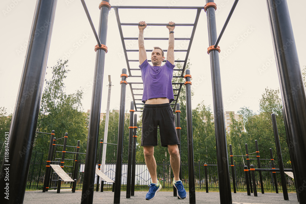 Naklejka premium Man practicing monkey bar exercise outdoors