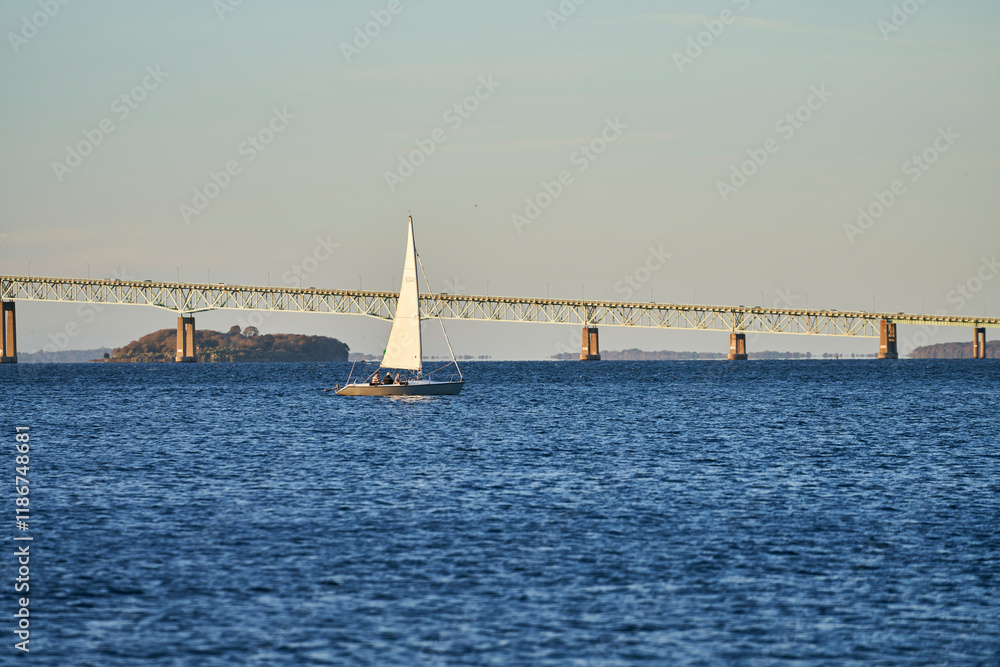 A sailboat navigates past the Claiborne Pell Newport bridge in beautiful blue ocean water. A sailboat navigates past the Claiborne Pell Newport bridge in beautiful blue ocean water.