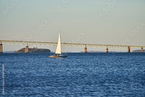 A sailboat navigates past the Claiborne Pell Newport bridge in beautiful blue ocean water. photo