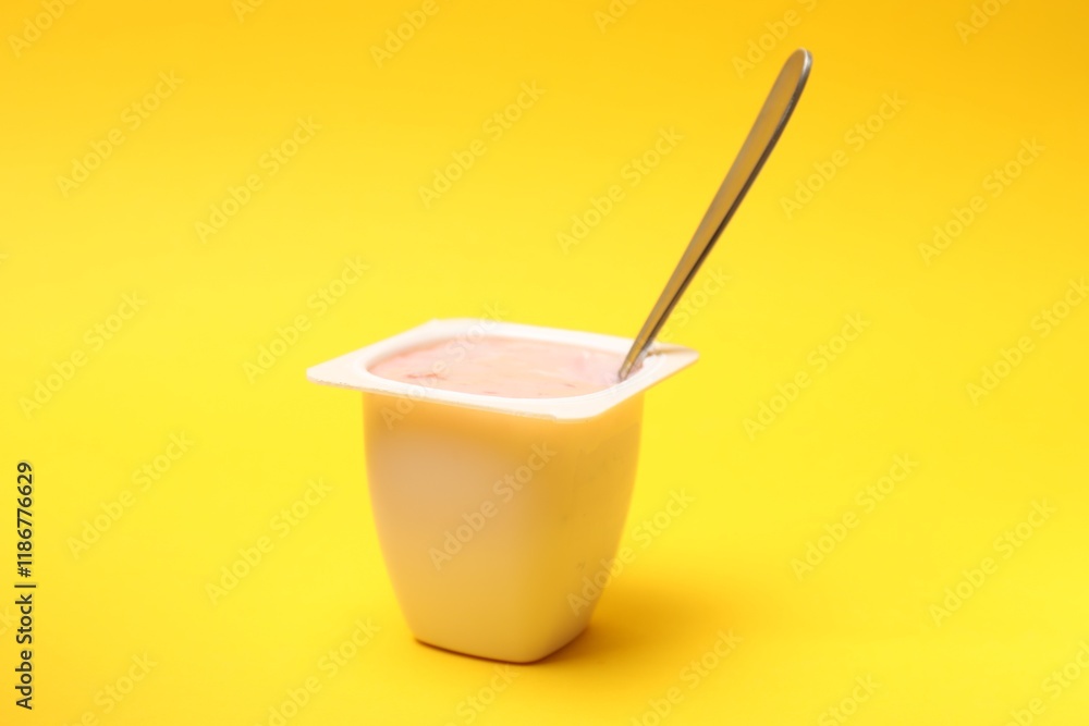 Delicious yogurt in plastic cup with spoon on yellow background Delicious yogurt in plastic cup with spoon on yellow background