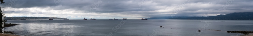 Cargo ships anchored in bay with boat leaving near shore of Stanley Park in Vancouver, BC, Canada. Cargo ships anchored in bay with boat leaving near shore of Stanley Park in Vancouver, BC, Canada.