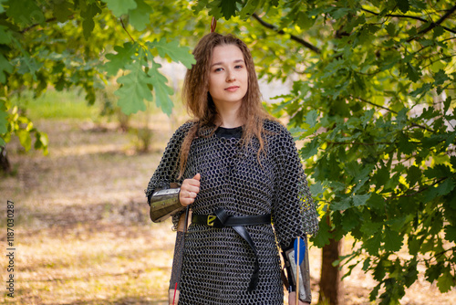 Medieval warrior woman in chain mail and bracers with a bow in her hands against the backdrop of an evening summer forest. photo