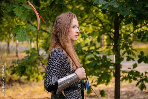 Medieval warrior woman in chain mail and bracers with a bow in her hands against the backdrop of an evening summer forest. photo