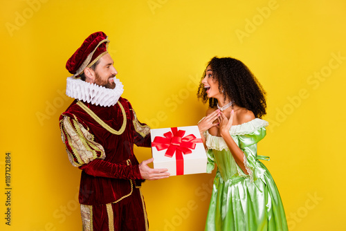 A joyful couple in elegant aristocratic costumes exchanging a gift against a vibrant yellow backdrop photo