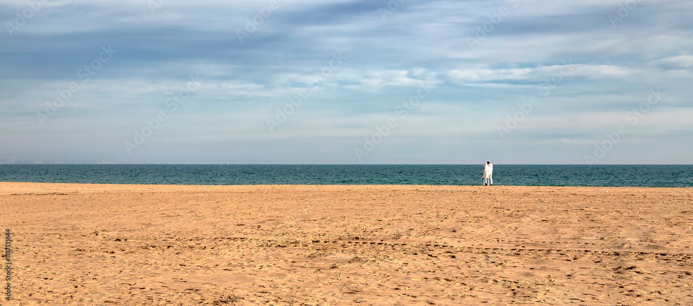 A couple wolking at a vast, sandy beach stretching towards the horizon