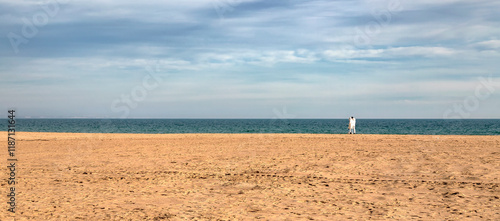 A couple wolking at a vast, sandy beach stretching towards the horizon photo