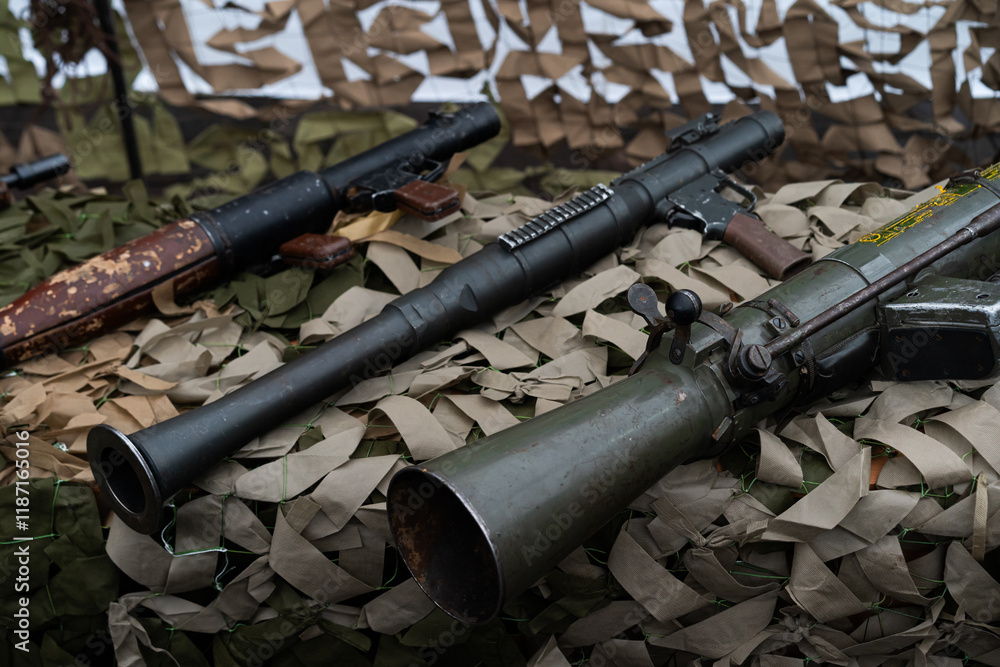 Fototapeta premium Display of various vintage firearms on camouflage netting at a military exhibition event