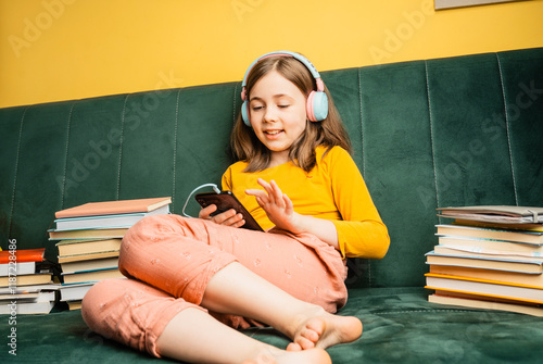 Smiling little caucasian girl in headphones have video call or distant class using her smartphon.Education or home schooling concept. School girl listens to an audio book. photo