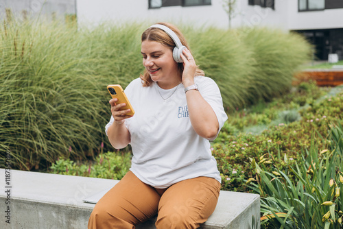 Closeup portrait of a lovely young female listening to music through wireless earphones on urban background. Music lover enjoying music. Woman record voice by mobile cell phone Dictaphone photo