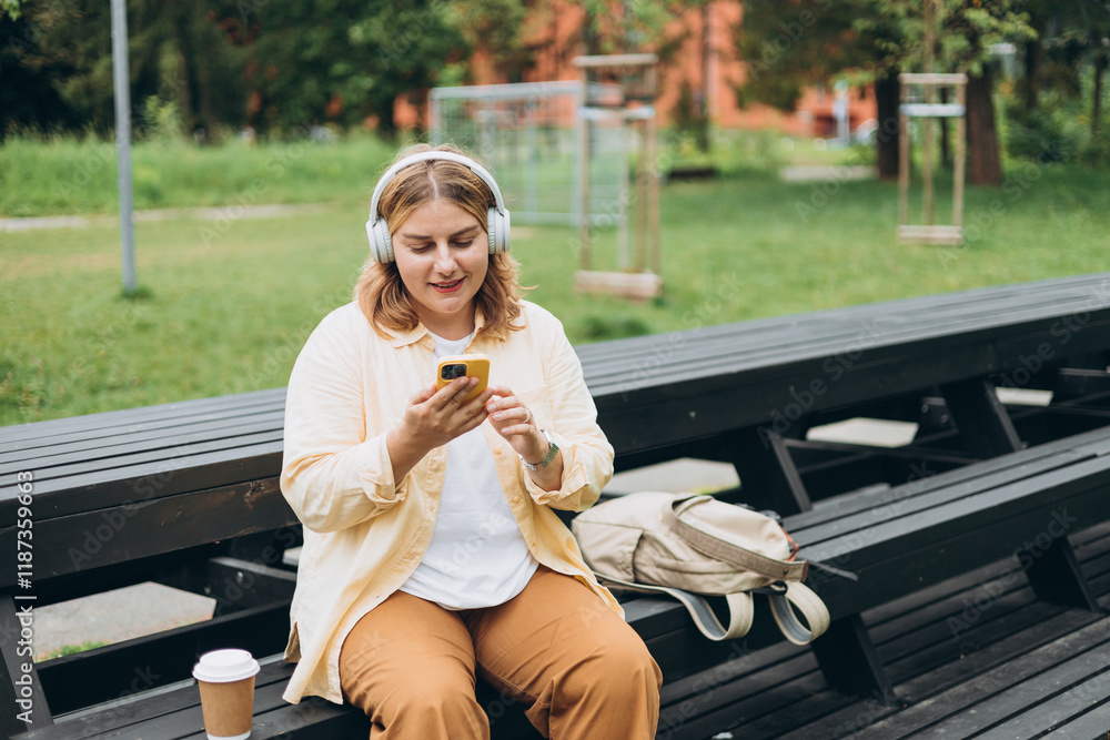 Closeup portrait of a lovely young female listening to music through wireless earphones on nature background. Music lover enjoying music. Woman record voice by mobile cell phone Dictaphone