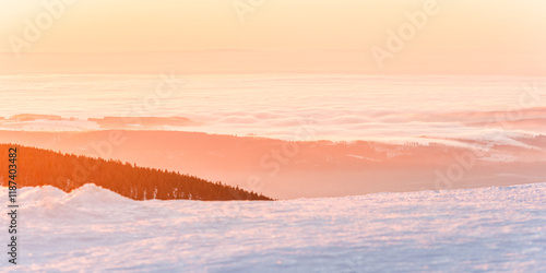 Fototapeta Naklejka Na Ścianę i Meble -  Eastern Sudetes, view of mountain range with thick fog in valley from peak from hiking trail during winter hike in mountains, viewpoint of wide winter landscape in mountains at orange sunset.