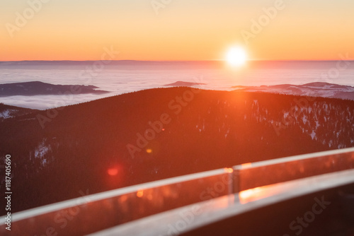Fototapeta Naklejka Na Ścianę i Meble -  Eastern Sudetes, view from the observation tower of the mountain range with thick fog in the valley from hiking trail during winter hike in mountains, winter landscape in mountains at orange sunset.