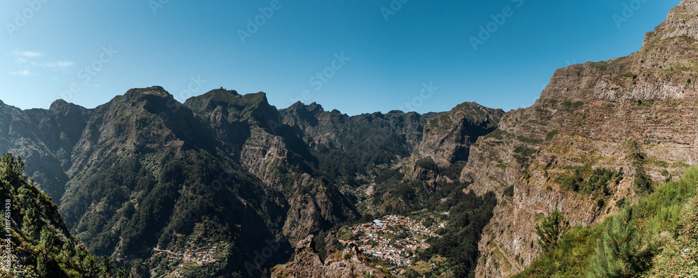 Obraz premium Panorama traditionelles Bergdorf auf Madeira – Panoramaaufnahme mit terrassierten Feldern und roten Ziegeldächern inmitten üppiger Natur bei strahlend blauen Himmel 
