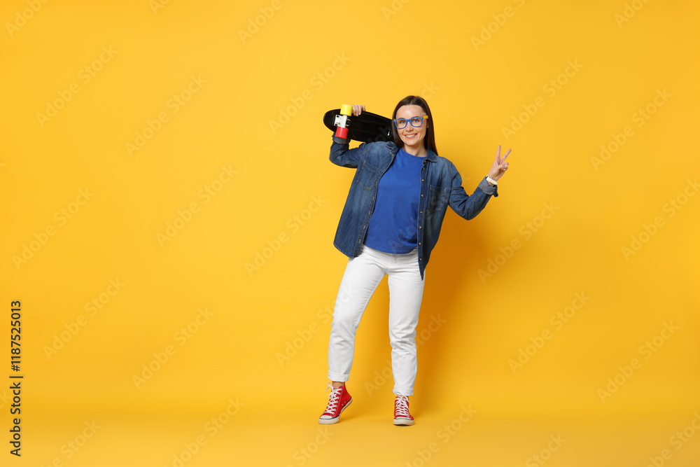 Smiling woman with penny board showing peace sign on orange background. Space for text Smiling woman with penny board showing peace sign on orange background. Space for text