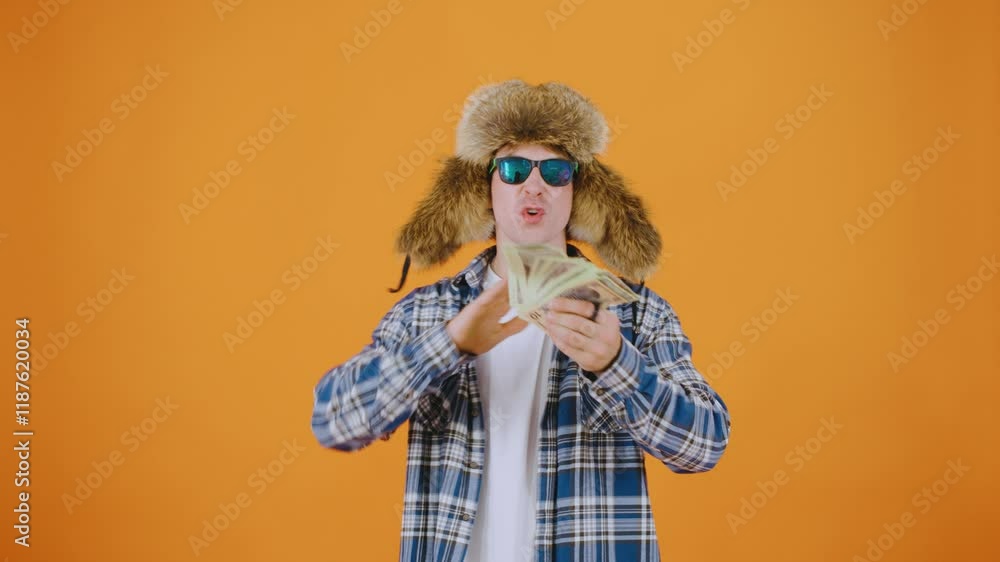 A man in sunglasses and a warm ushanka hat joyfully throws dollar bills while saying A man in sunglasses and a warm ushanka hat joyfully throws dollar bills while saying