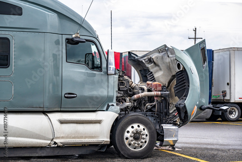 Broken gray big rig semi truck with open hood standing on the truck stop parking lot waiting for qualified repair