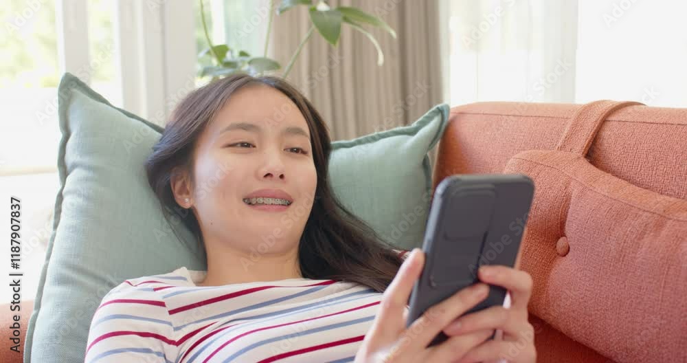 Smiling asian teenage girl lying on couch using tablet for entertainment and relaxation Smiling asian teenage girl lying on couch using tablet for entertainment and relaxation
