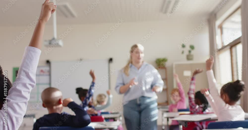 In school classroom, students raising hands while female teacher ...