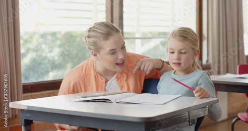 In school, female teacher smiling and helping young student with homework at desk photo