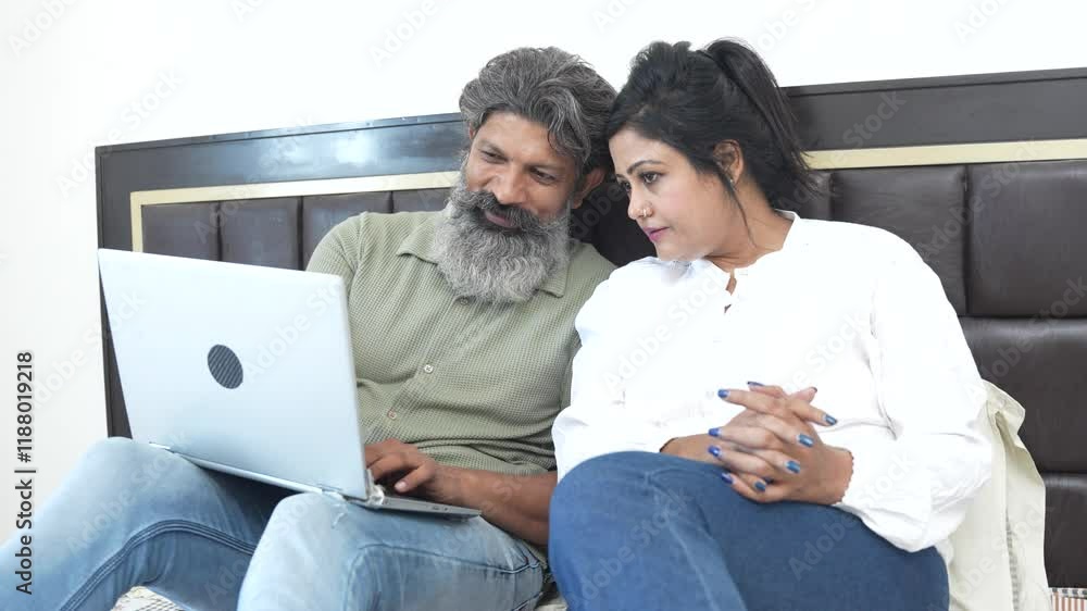Mature indian couple using laptop while sitting in bed at home. Husband wife web surfing interest online together. watching video, Wireless technology. Domestic life, Relationship bonding. Mature indian couple using laptop while sitting in bed at home. Husband wife web surfing interest online together. watching video, Wireless technology. Domestic life, Relationship bonding.