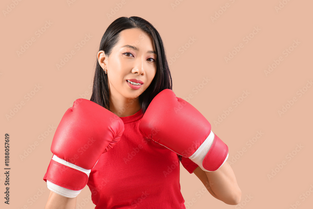 Beautiful young Asian woman in boxing gloves on beige background. Women history month Beautiful young Asian woman in boxing gloves on beige background. Women history month