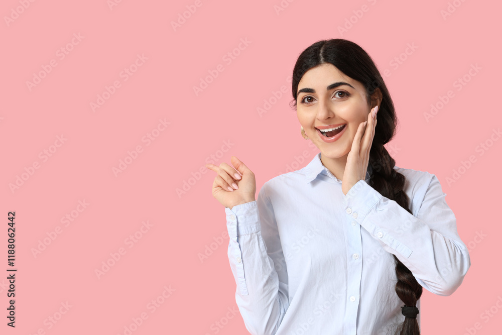 Beautiful young happy Indian woman pointing at something on pink background Beautiful young happy Indian woman pointing at something on pink background