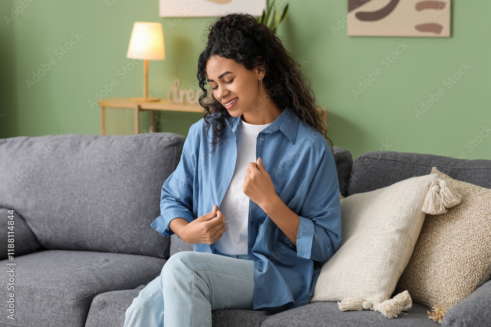 Φωτογραφία Pretty young African-American woman in stylish blue shirt sitting on sofa at hom