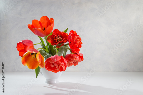 A bouquet of red tulips in a white vase on a light background. Copy space photo