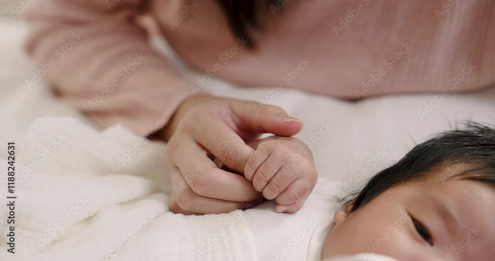 Closeup of baby’s tiny hand held by mother’s hand on white blanket. Symbolizes security, tenderness, nurturing connection, and the intimate bond of mother and child in early life. Closeup of baby’s tiny hand held by mother’s hand on white blanket. Symbolizes security, tenderness, nurturing connection, and the intimate bond of mother and child in early life.