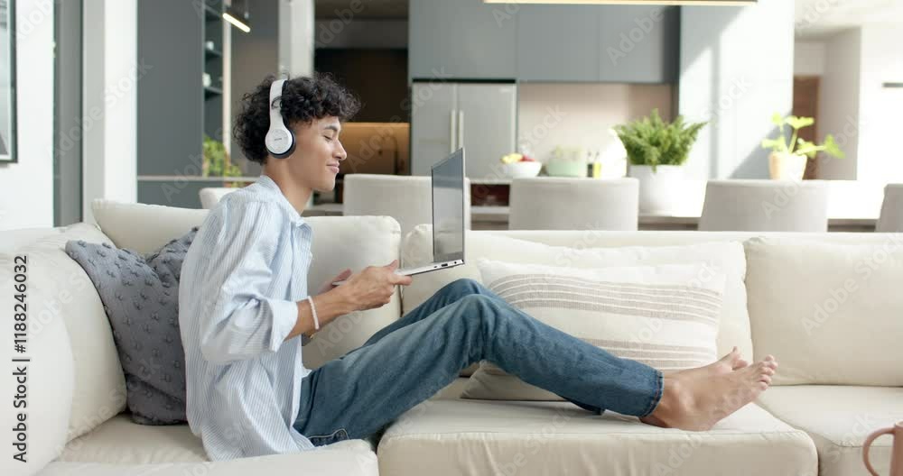 Relaxing on sofa, teenage boy using laptop and wearing headphones at home Relaxing on sofa, teenage boy using laptop and wearing headphones at home