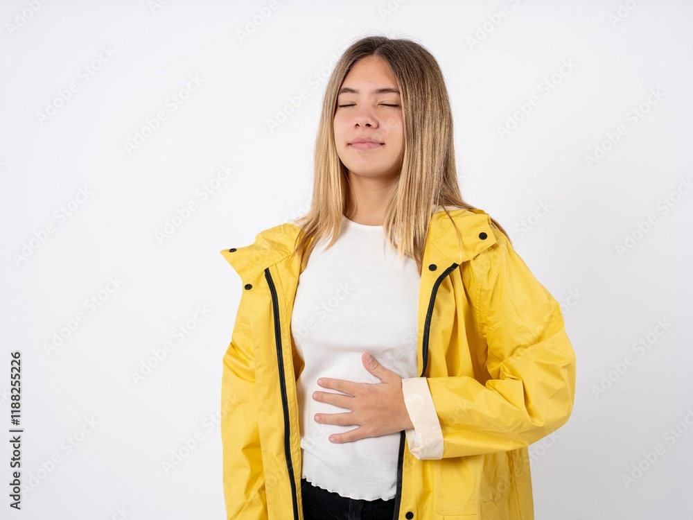 Beautiful teen girl wearing rain coat touches tummy, smiles gently, eating and satisfaction concept. Beautiful teen girl wearing rain coat touches tummy, smiles gently, eating and satisfaction concept.