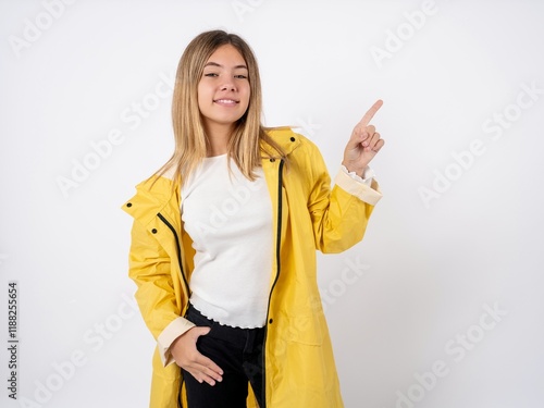 Beautiful teen girl wearing rain coat looking at camera indicating finger empty space sales