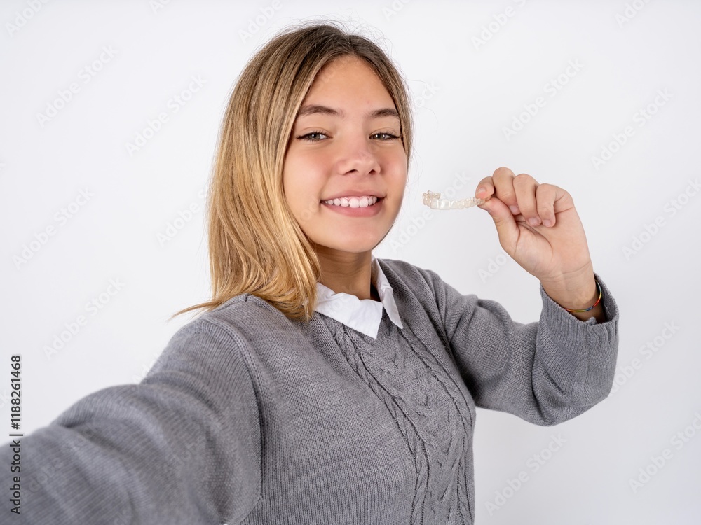 Beautiful teen girl wearing grey sweater make selfie holding an invisible braces aligner, recommending this new treatment. Dental healthcare concept. Beautiful teen girl wearing grey sweater make selfie holding an invisible braces aligner, recommending this new treatment. Dental healthcare concept.
