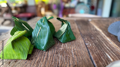 Traditional Asian desserts wrapped in fresh green banana leaves, neatly folded and secured with toothpicks, placed on a rustic wooden table in a cozy setting.