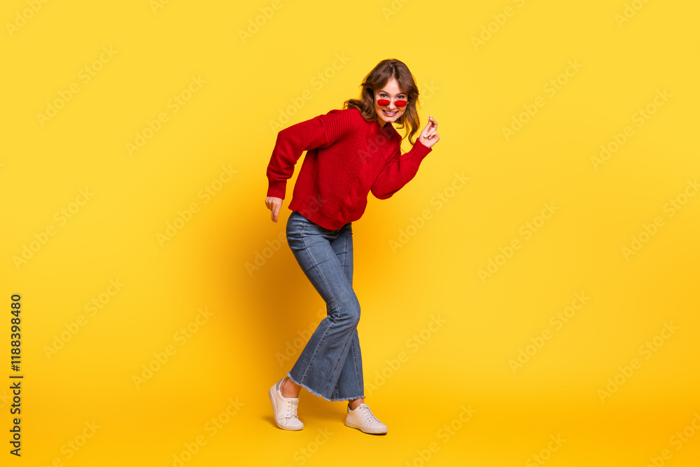Fototapeta premium Cheerful young woman in trendy red sweater dancing against a vibrant yellow background, showcasing stylish casual wear