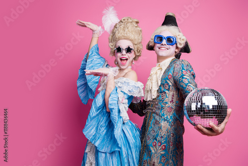 Energetic couple in baroque costumes poses joyfully against a vibrant pink background, capturing the essence of a themed carnival photo