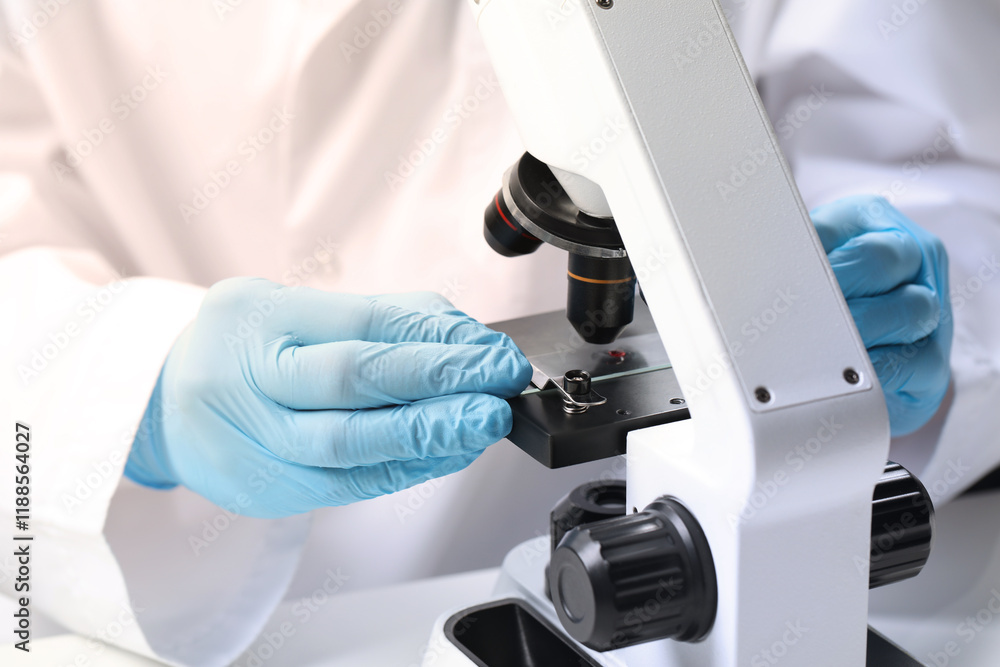 Scientist examining sample on slide under microscope at table, closeup Scientist examining sample on slide under microscope at table, closeup