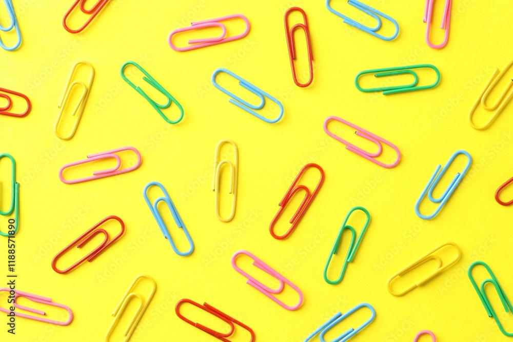 Colorful paper clips on yellow background, flat lay Colorful paper clips on yellow background, flat lay