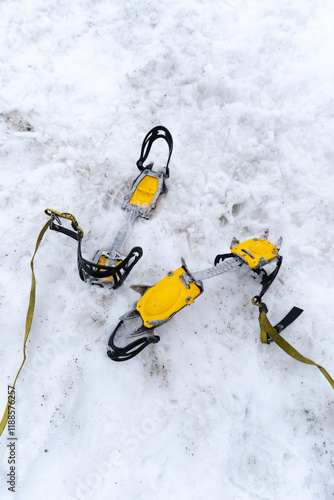 Iron crampons with yellow details lying in the snow, , ready for ice climbing or mountaineering photo