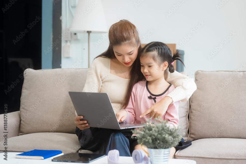 Asian young mother and her daughter sit together on the sofa in the cozy living room, working on homework at the desk, creating a warm and supportive atmosphere for learning, love, hug, mother days. Asian young mother and her daughter sit together on the sofa in the cozy living room, working on homework at the desk, creating a warm and supportive atmosphere for learning, love, hug, mother days.