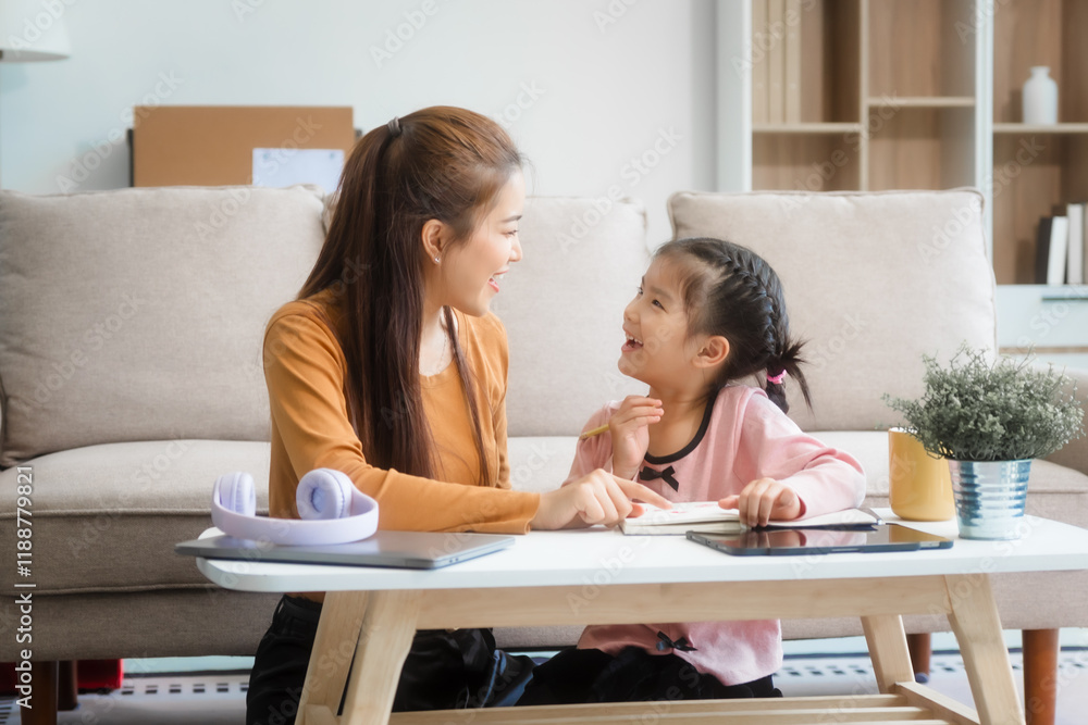 Asian young mother and her daughter sit together on the sofa in the cozy living room, working on homework at the desk, creating a warm and supportive atmosphere for learning, love, hug, mother days. Asian young mother and her daughter sit together on the sofa in the cozy living room, working on homework at the desk, creating a warm and supportive atmosphere for learning, love, hug, mother days.
